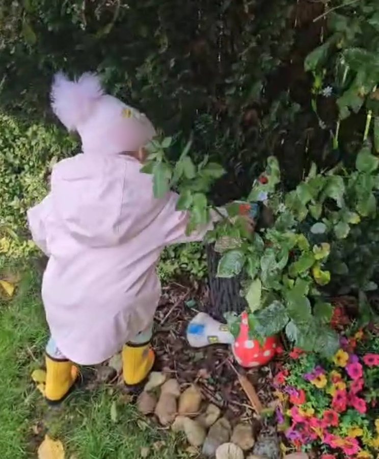 A child in a pink coat and yellow boots at the fairy garden, seen from behind